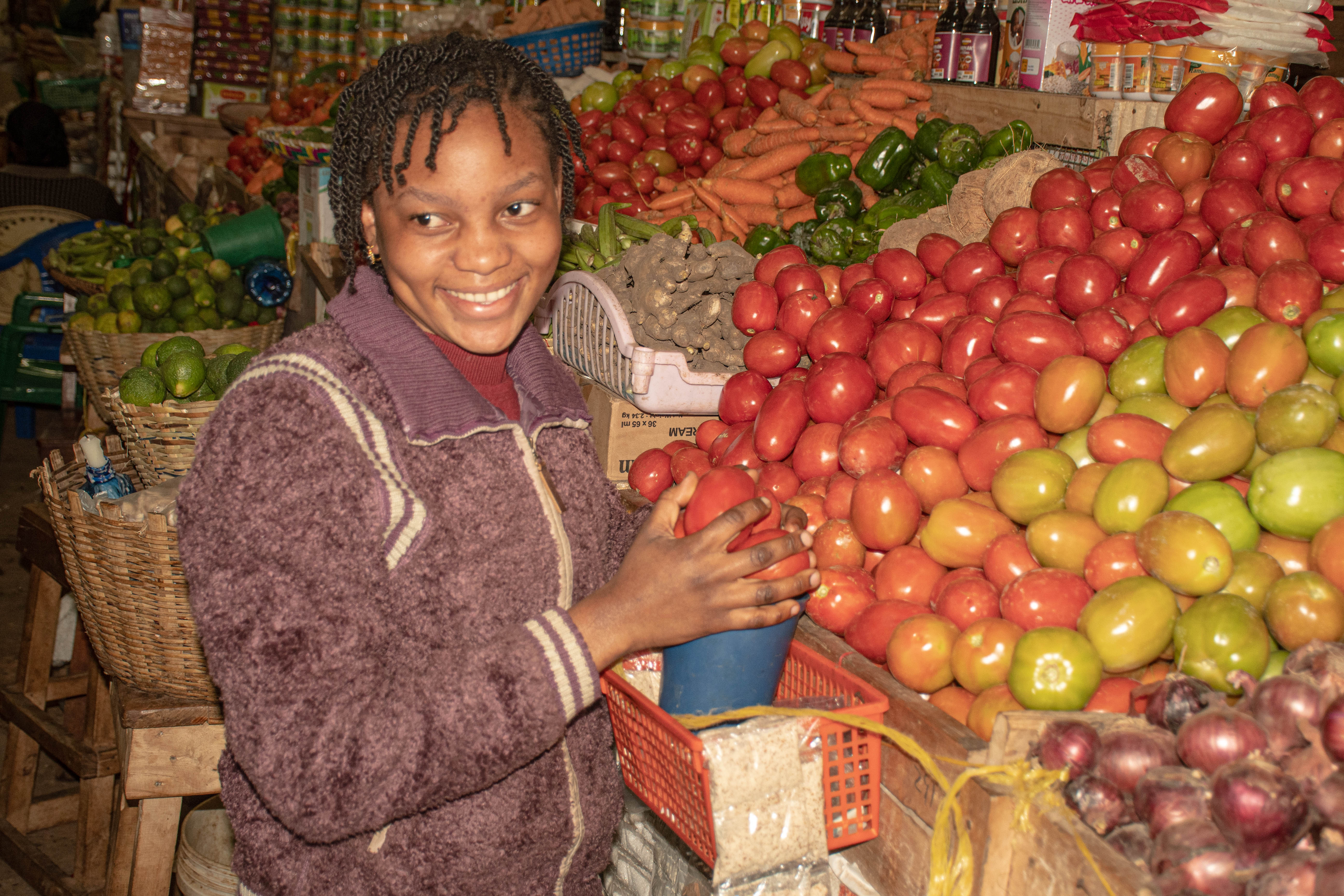A young woman smallholder farmer and trader from Njombe Market selling a variety of fresh vegetables. 