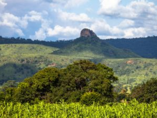 Lush green hills with a rocky mountain peak rising in the distance under a partly cloudy sky.